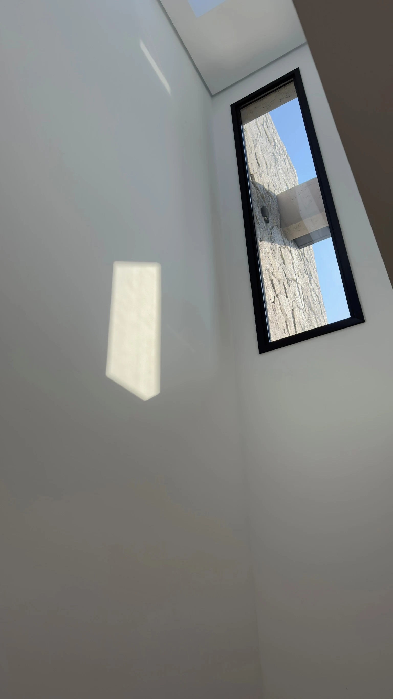 Tall stairwell with a narrow window framing the exterior stone chimney and blue sky